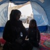 Woman and little girl sitting inside of a blue tent in Syria