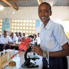 A young woman in a classroom standing beside a microscope.