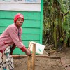 A woman in a pink sweater washing her hands at an outdoor tap in DRC