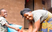 Ethel Nkhoma washes her hands above a bucket of water while her son Chisomo sits beside her.