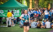 A woman smiles and walks towards the camera after crossing the London Marathon finish line. She is wearing her finisher medal and a Concern branded running vest in green and pink with her name written on the front.
