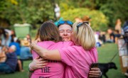 A woman smiles tearfully and embraces 2 female family members, both wearing pink, after crossing the finish line.