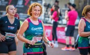 A woman smiles proudly whilst running toward the finish line. She is wearing a Concern branded running vest in green and pink with her name written on the front. She is surrounded by other runners.