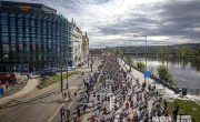 Participants for the Prague Half Marathon run on the course. All runners are wearing different colours running vests including black, blue and red. The course is next to open water and spectators watch on.