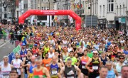  Hundreds of runners cross the start line for the Cardiff Half Marathon. All runners are wearing different coloured running vests including white, red, yellow and blue. The start line arch is red and reads ‘Principality of Building Society – Cardiff Half’