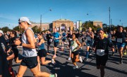 Participants for the Copenhagen Half Marathon run on the course. They are wearing different coloured running vests including black, blue and white.  