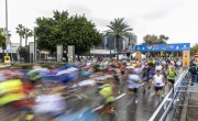 Hundreds of runners cross the start line for the Valenica Half Marathon. The runners are blurry due to movement and there are hundreds more still waiting to start. The weather is gloomy. 