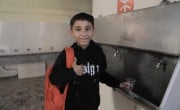 A boy in front of a sink holding a cup