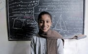 A young girl stands in front of a blackboard
