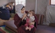 A woman gives a small child a cup of water to drink