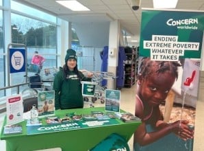 Person standing at a Concern Worldwide display table with brochures and signage about ending extreme poverty.