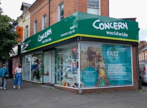 Concern Worldwide charity shop on a street corner with green signage, large window displays, and promotional posters.