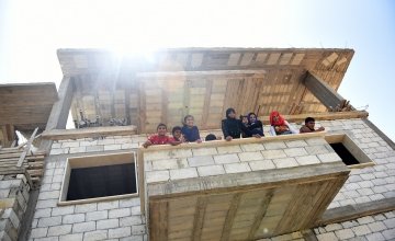 Syrian refugees lean out of the balcony of the home in Northern Lebanon where Concern will be putting in doors and windows into the family's home. Photograph by Mary Turner