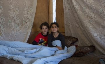 Two Syrian refugee children sit under a duvet