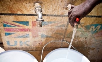A hand runs a tap against the background of a UK aid logo