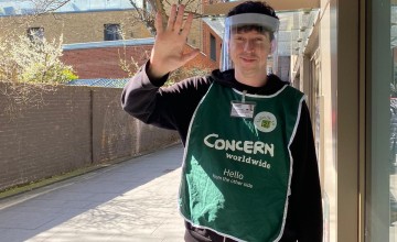 Street fundraiser in protective gear smiles and waves 