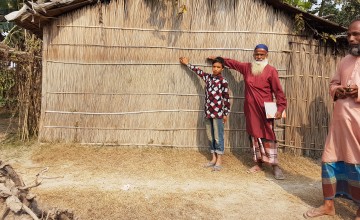 A Bangladeshi man and boy show the level of the flood waters reached by a 2019 monsoon relative to their home.