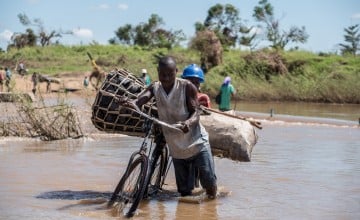 Man pushing his bicycle through a flooded river in Mozambique after Cyclone Idai