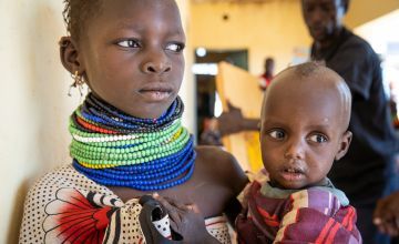 Ngirethi  holds her younger sister, Mary, as they wait to be screened for malnutrition at Sasame Dispensary.