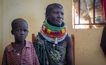 Kenyan woman in colourful beaded necklaces sitting next to small boy in striped t-shirt