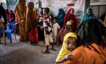 Infant girl holding onto mother's shoulder and being carried in Somalian health centre