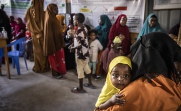Infant girl holding onto mother's shoulder and being carried in Somalian health centre