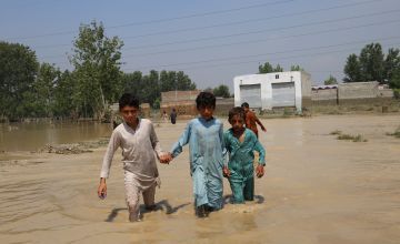 Three boys holding hands and walking through floodwater in Pakistan