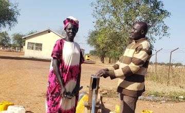 Two people stand at a hand pump