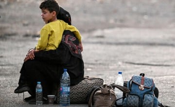 A woman sits with a child on her lap next to bags on the ground as people flee from Lebanon. Photo by LOUAI BESHARA/AFP via Getty Images