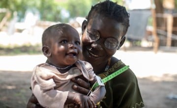 Alekiir and her daughter Achol wait outside a Concern nutrition center in Lueth Ngor, Northern Bahr el Ghazal State, South Sudan. While they wait, Alekiir measures Achol's mid-upper-arm circumference (MUAC) to check her nutrition levels. (Photo: Jon Hozier-Byrne/Concern Worldwide)