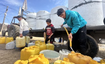 Boys in Gaza collect clean water from large white tanks on a truck, filling yellow