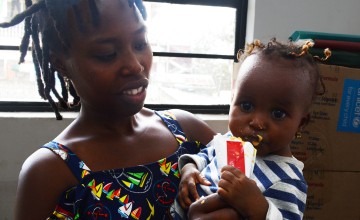 Alt text: A woman looks at her daughter eating a therapeutic food sachet while looking at the camera. 