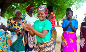 People dressed in brightly coloured clothes dance under a tree smiling