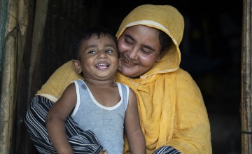 A mother wearing yellow looks down smiling at her young son.