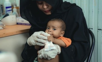 A baby is held by a woman and fed food from a package
