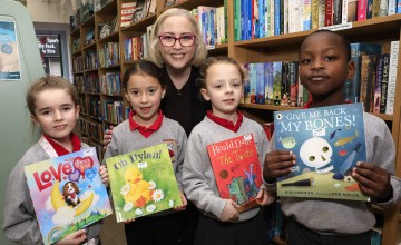 Four children holding books alongside a woman