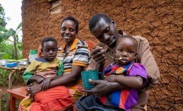 A couple sit next to one another with their children, the man is feeding one of the children.