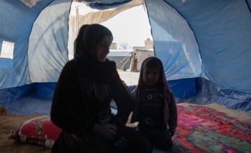 Woman and little girl sitting inside of a blue tent in Syria