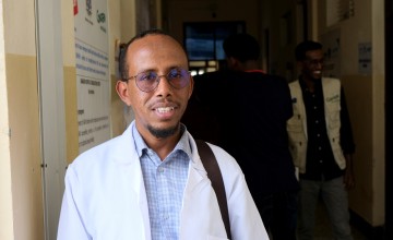 Man with glasses and a white jacket stands in a doorway