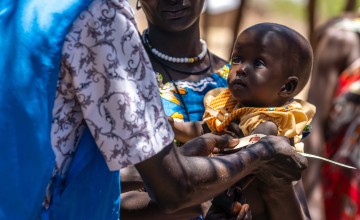 Woman holds a baby in her arms who is being measured with a MUAC band