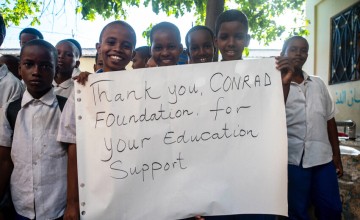 Group of schoolchildren holding a handwritten sign thanking a foundation for education support.