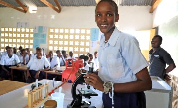 A young woman in a classroom standing beside a microscope.