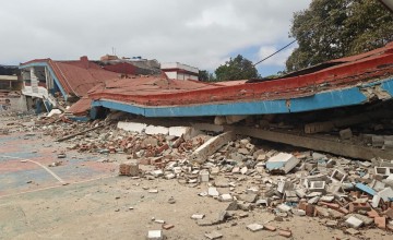 Collapsed building and piles of rubble cover a school playground after earthquake damage.
