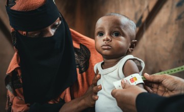 Child’s upper arm being measured with a nutrition screening tape while seated beside a caregiver