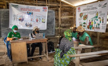 Concern staff sitting behind a desk speak with a woman in a green dress in DRC