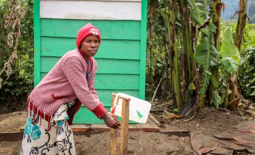 A woman in a pink sweater washing her hands at an outdoor tap in DRC