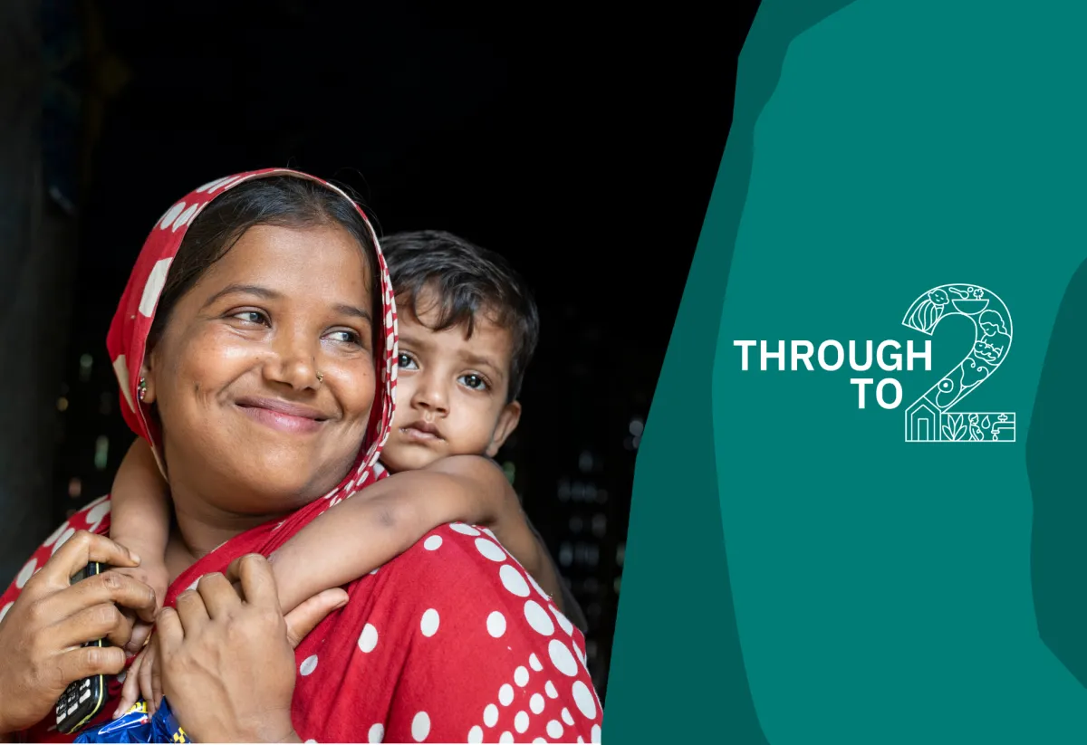 A close-up portrait of a smiling woman in a red patterned headscarf carrying a young child on her back. The child rests an arm around her shoulders and looks towards the camera. On the right, a teal panel features the "Through to 2" campaign logo.