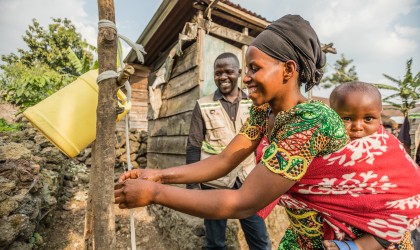 Apoline washes her hands at a Concern-installed handwashing station in Kitshanga, while Concern community worker Abel watches on. Photo: Pamela Tulizo / Panos / Concern Worldwide