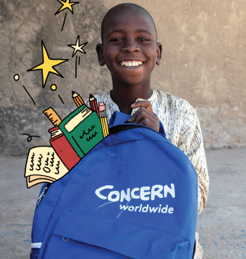 A smiling boy holds a blue Concern Worldwide backpack, surrounded by illustrated books, pencils, a ruler and yellow stars.