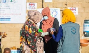 Three woman stand in front of a wall with UK Aid signs